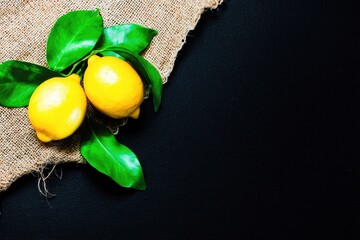 Two ripe lemons with leaves on burlap against a dark background