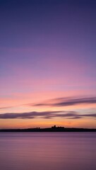 Obraz premium Dramatic Sunset Sky Over Calm Water and Distant Castle Silhouette