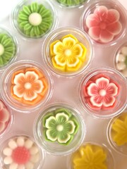 Colorful flower-shaped jelly desserts in clear cups, artistically arranged with vibrant floral designs and intricate petal details.