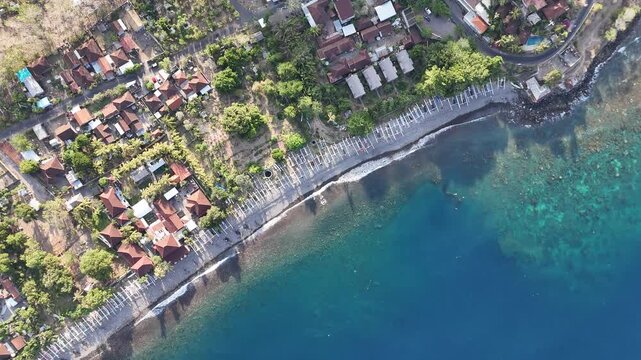 Aerial view of a tropical beach with bungalows, palm trees, and fishermen boats on the ocean coast in Amed, Bali