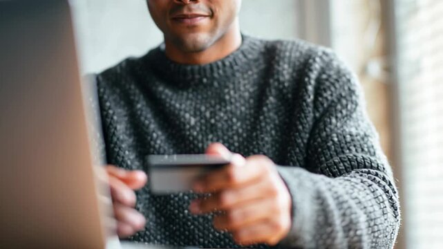 Holding payment card while using laptop, focused on online transaction process, cozy setting