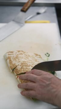Vertical video. Cutting pita sandwich. Cooking burrito. Chef serving by knife piece grilled stuffed flatbread with vegetable. Hands preparing hot street food.