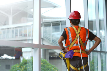 A construction worker in safety gear and helmet stands by a glass wall, looking outside while wearing a harness for protection. © Daniel Pawer