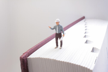 Fototapeta premium Miniature Engineer Standing On a Large Book Representing Knowledge