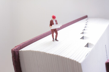 Obraz premium Miniature Worker Standing on a Book Holding Blueprints
