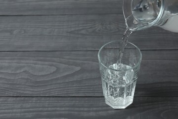 Pouring water from jug into glass at wooden table, closeup. Drinking clear water in the morning for health. Space for text 