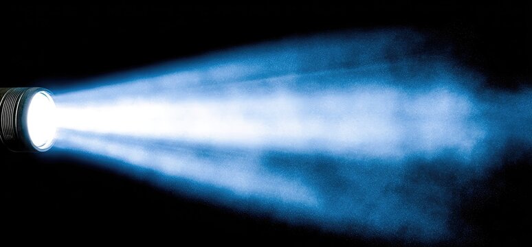 A powerful beam of light radiates outward from a flashlight, illuminating the darkness with bright blue tones.