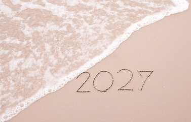 2027 year handwritten with ocean waves on a sandy beach. New Year 2027 concept