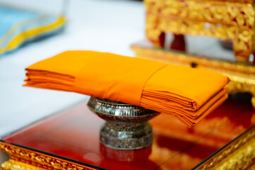 Close-up of a stack of orange monk's robes, neatly folded on an ornate silver pedestal, with other...