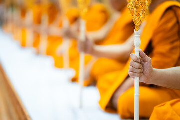 A close-up of a monk's hand holding a ceremonial staff with other monks in the background, blurred.