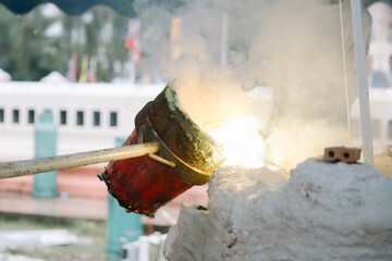 A close-up shot of a crucible containing what appears to be molten metal, held by a long handle, suggesting a process of casting or smelting.