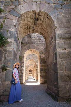 Asian woman tourist take a holiday for travel in summer at Acropolis of Pergamon Ancient Greek City, Landmark of Tourism Turkiye, Izmir, Turkey. She is standing archway area and enjoy relax vacation.