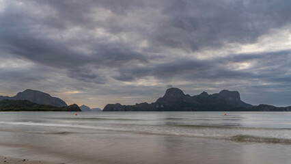Evening on a tropical island. Blue clouds in the sky. Silhouettes of mountains on the horizon. Ocean waves are spreading across the sandy beach. Long exposure. Philippines. Palawan. El Nido.
