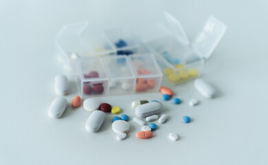 A variety of colorful medicine or pills and tablets with a weekly pill organizer represent daily...