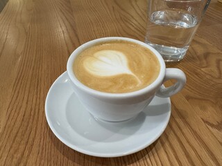 Side view of hot latte coffee with latte art in white cup on wooden table