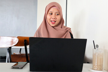 An Asian Muslim woman is seriously working on a laptop.