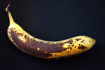 Close-up of one ripe brown banana on a black background with copy space.