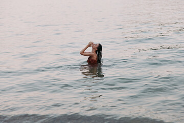 A person stands waist deep in calm water, tilting head back as hands frame the face, capturing a...