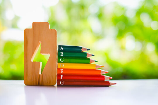 Energy efficiency rating concept with colorful pencils labeled A to G next to wooden battery icon. Symbol of power saving, green energy, sustainability, eco-friendly lifestyle, and environment.