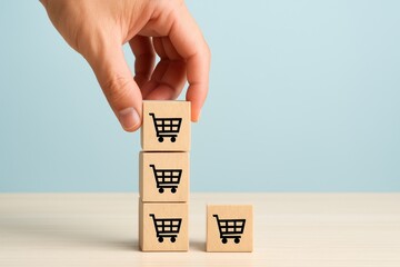 Hand Placing Wooden Blocks with Shopping Cart Icons on a Light Blue Background for E-Commerce and Retail Concept