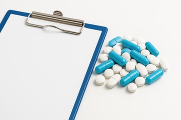 Medical Clipboard with Blank Sheet and Assorted Blue and White Pills on a Clean Surface, Concept of Healthcare and Pharmacy