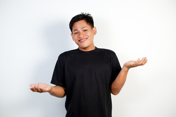 Portrait of a young Asian man in black shirt shrugging with a confused face against a white...