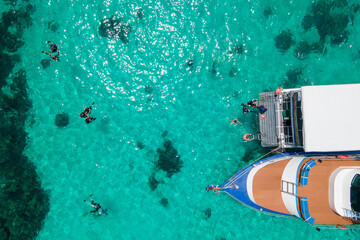 Aerial view of scuba divers swimming on water surface and climbing up on boat platform at Koh Racha...