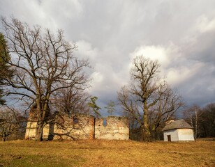 Fototapeta premium Atmospheric scene with the ruins of a historical building next to a small white chapel in a rural landscape. Captured during late autumn or early spring in the countryside of Slovakia.