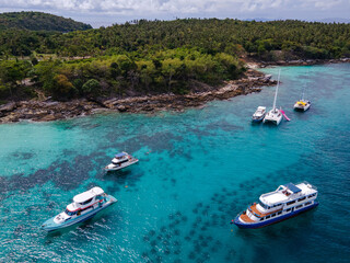 Fototapeta premium Aerial view of Koh Racha Yai Island with many tour boats, yacht, catamaran and longtail boat anchoring around the bay. A popular destination for summer vacation in Phuket, Thailand.