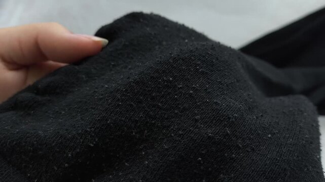 Black pellets, lint on black clothes close-up. Removing pellets from clothes.