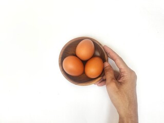 A person's right hand is holding a wooden saucer with fresh chicken eggs against a white background.