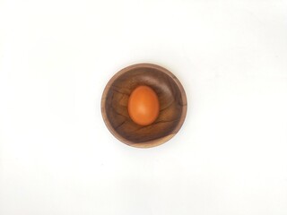 Top view of a fresh chicken egg in a wooden saucer on a white background