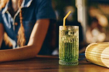 Lifestyle woman in modern boho-western denim street style with a refreshing drink on the bar in warm film color lighting, casual and relaxed vibe.