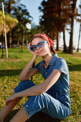 Naklejka premium lifestyle woman in modern boho-western denim street style wearing blue sunglasses and red bandana outdoors in warm sunlight with film color effect