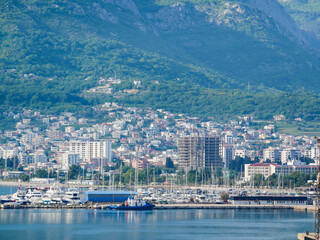 Fototapeta premium Scenic view of yacht club and marina in Bar, Montenegro, with boats, city buildings, and mountains in the background.
