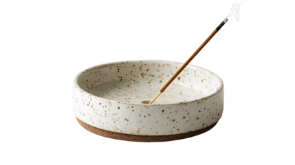 A round, shallow ceramic incense burner, speckled with light brown flecks, sits on a dark-brown ring. A light-brown incense stick is centered in the bowl