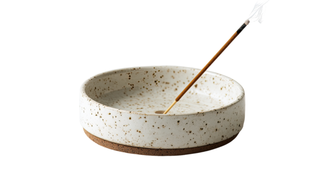 A round, shallow ceramic incense burner, speckled with light brown flecks, sits on a dark-brown ring. A light-brown incense stick is centered in the bowl