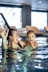 Mom holding baby in spa pool, finger near mouth. Vertical portrait.