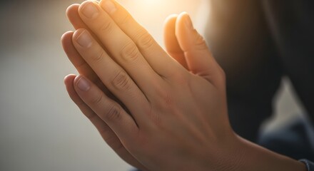 Close up of person praying with hands together illuminated by warm sunlight