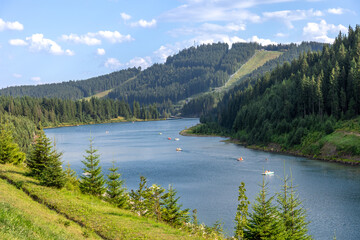 Mountain lake with paddle boats and pine slopes. Summer leisure on water.