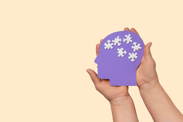 Hands hold a purple head silhouette featuring white puzzle pieces