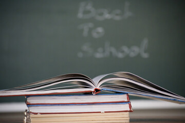 Open book on top of a stack of books with a chalkboard background.