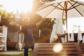 Worker opening parasol in a resort at sunset