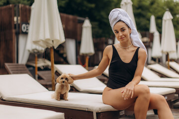 Young woman petting her dog by the poolside after shower