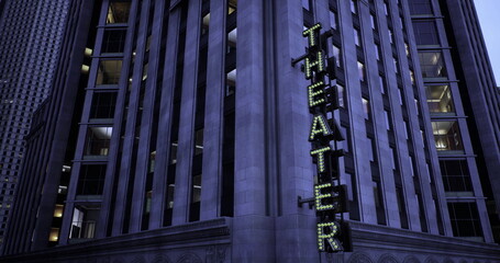 Obraz premium A historic theater building stands prominently in the city as the evening sky darkens. Neon lights spell out the word theater, attracting attention from passing pedestrians.