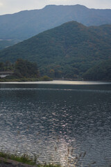 Light shines on a blue lake below a mountain full of trees.
