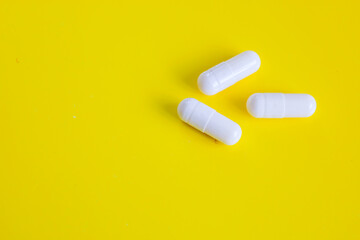 Three white capsules with blurry inscriptions are arranged on a bright yellow background. This minimalistic shot emphasizes the simplicity, purity, and importance of medical preparations in the health