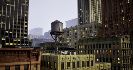 A historic water tower is prominently placed atop a yellow building, surrounded by skyscrapers under a dusky sky, showcasing the blend of architecture and urban life after sunset.
