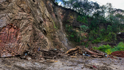 Fototapeta premium A rocky cliff with landslide debris, fallen trees, and mud after heavy rain, showing the impact of natural disaster and erosion.