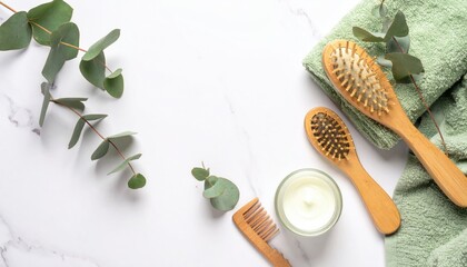 Marble surface showcasing two wooden hair brushes, comb, eucalyptus sprigs, sage-green towel, and a candle; calm and natural flat lay